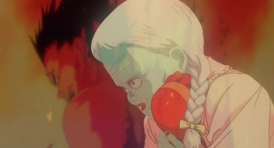 Akira (1988) movie still: closeup — A surreal animated scene featuring a woman with white hair and a dark-haired man. The woman holds a red…
