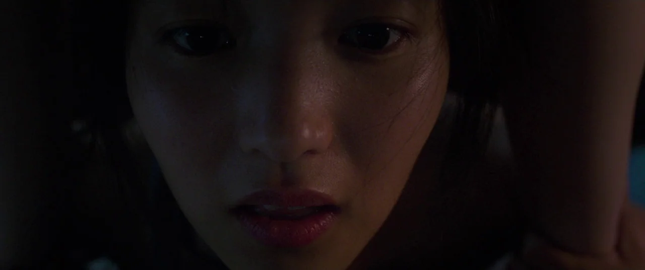 The Handmaiden (2016) movie still: closeup — A dark, undifferentiated environment surrounds the subject in a tight frame. A young woman looks…