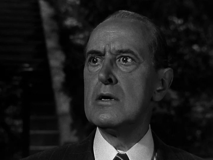 Nightmare Alley (1947) movie still: closeup — An older man stands outdoors at night near a stone stairway in shadow. The man gazes forward with a…