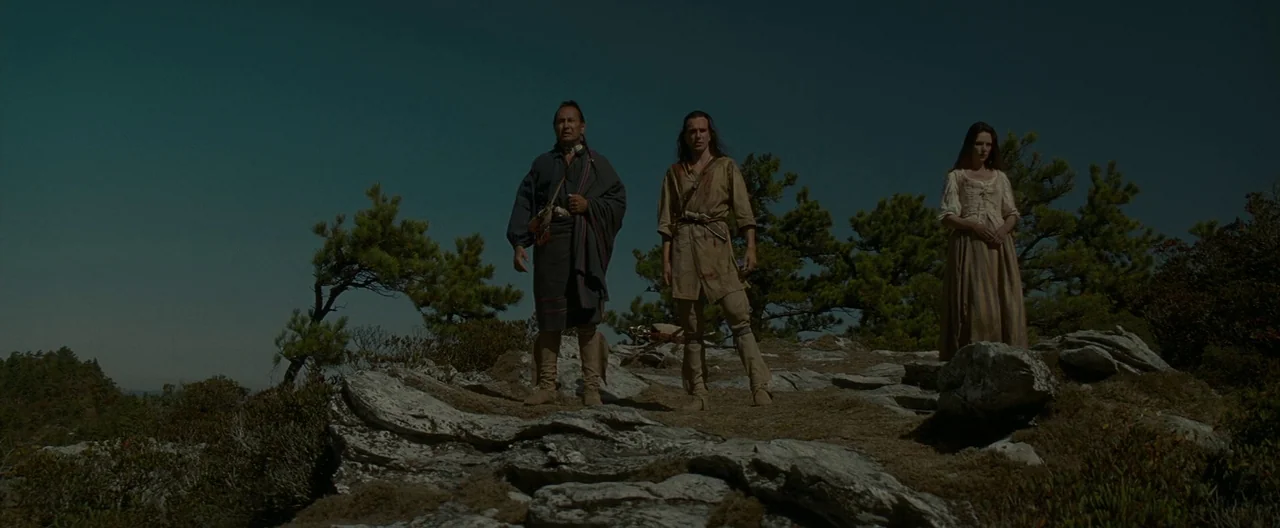 The Last of the Mohicans (1992) movie still: fullbody — A rocky mountain peak overlooks a vast, clear landscape under a dark sky. Three figures…
