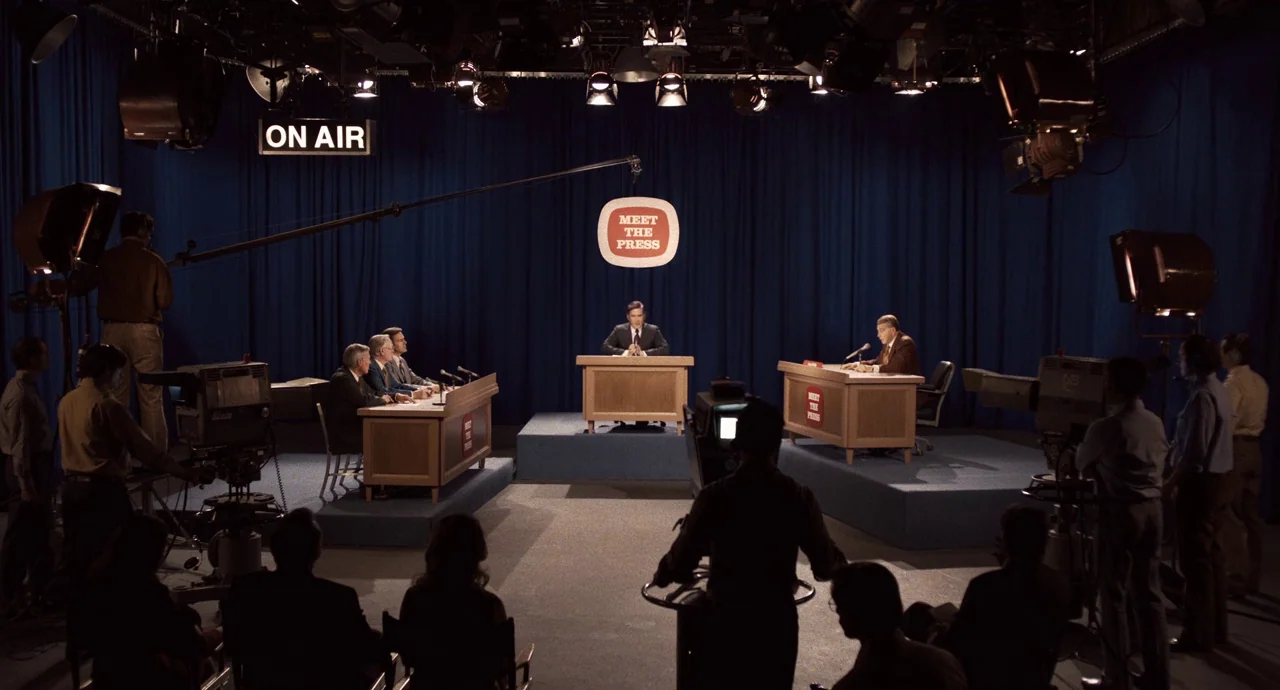 The Irishman (2019) movie still: wide — A television broadcast studio features dark blue curtains and professional news desks on risers. Camera…