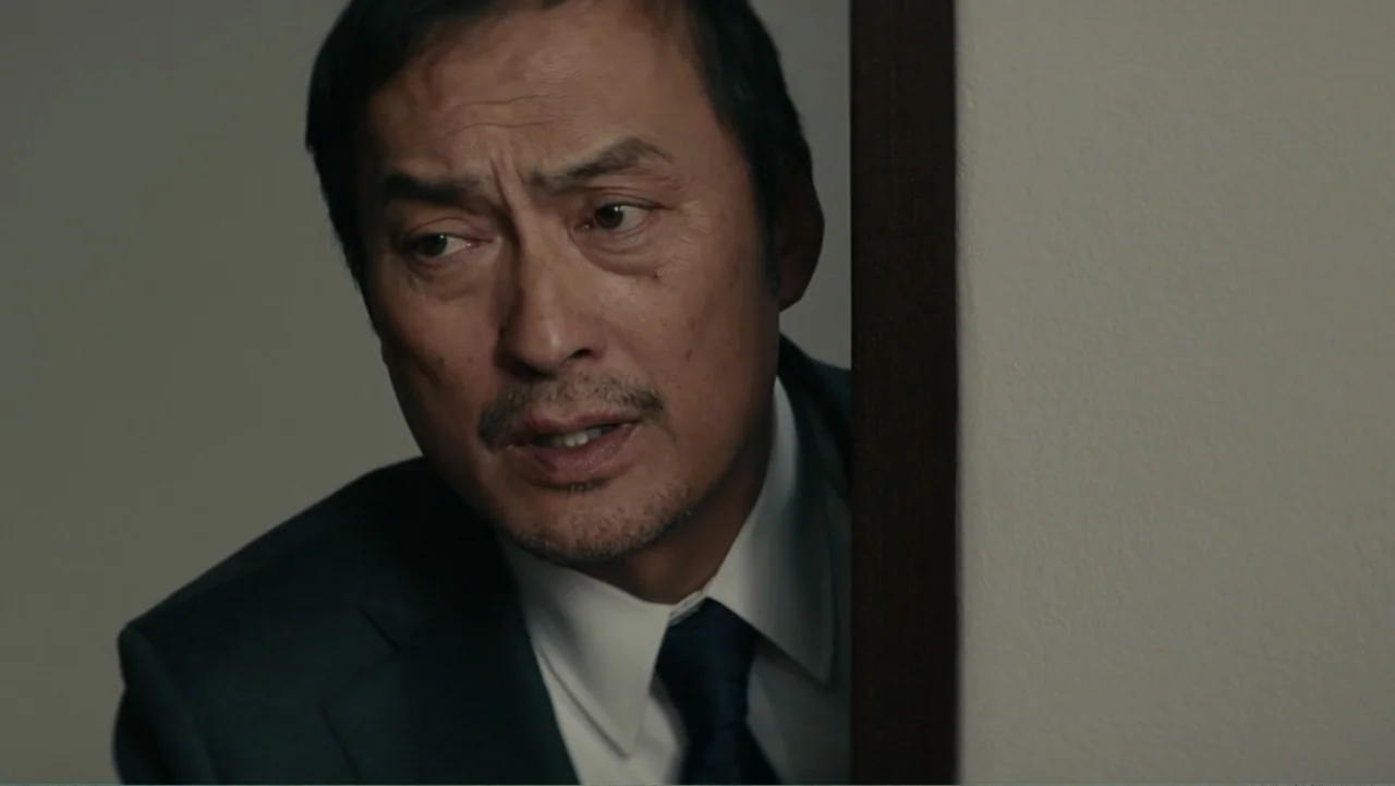Bel Canto (2018) movie still: closeup — A man peers from behind a doorway in a dimly lit, minimalist interior setting. The subject, a man in his…