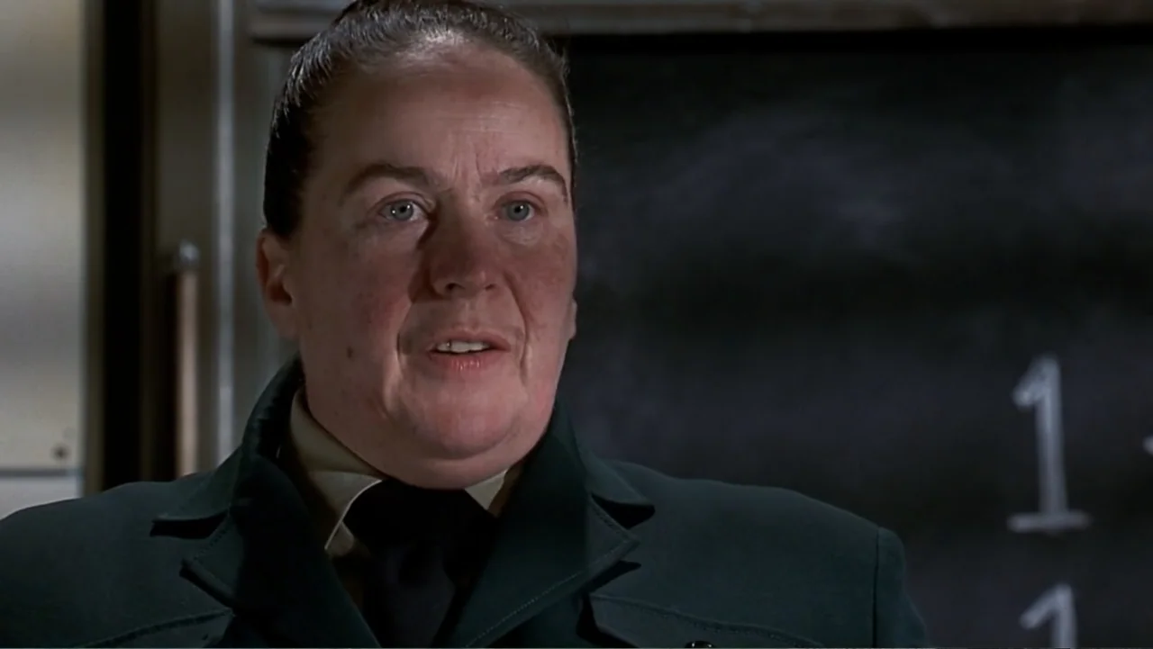 Matilda (1996) movie still: closeup — A dark, blurred interior space features a chalkboard with faint white markings behind the subject. A…