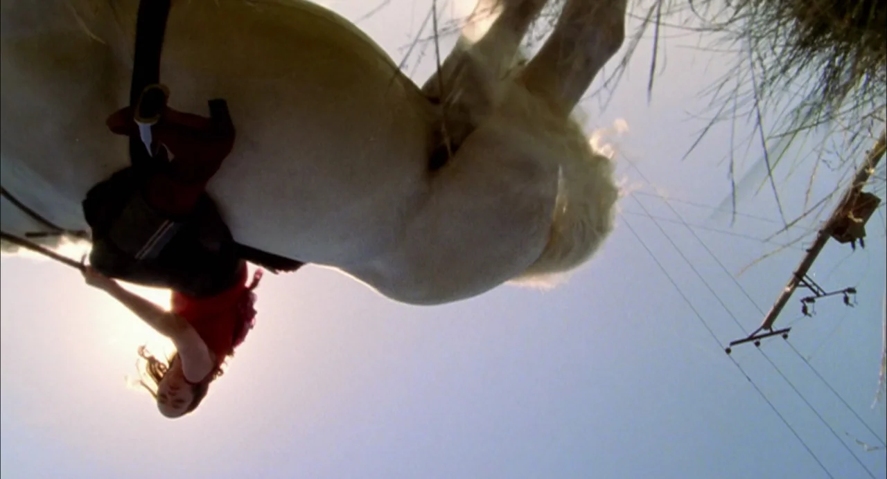 My Summer of Love movie still: wide — An open field under a clear blue sky during a sunny day. A woman rides a white horse while seen from a low…