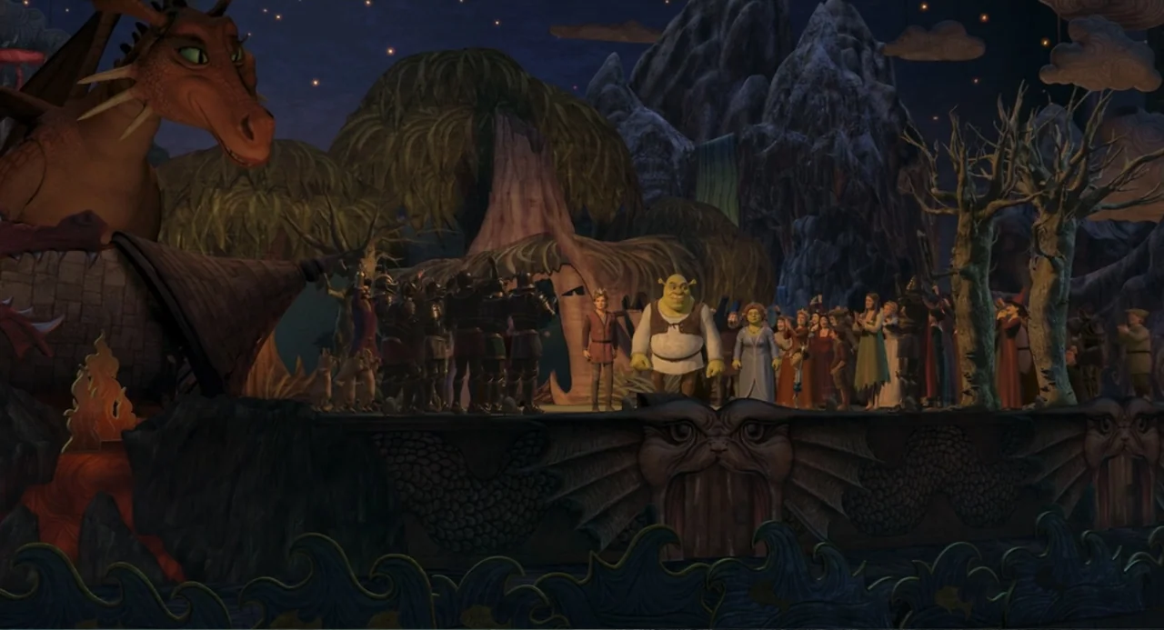 Shrek the Third (2007) movie still: wide — A dark night scene features an outdoor stage decorated with oversized dragon and tree props. Shrek and…