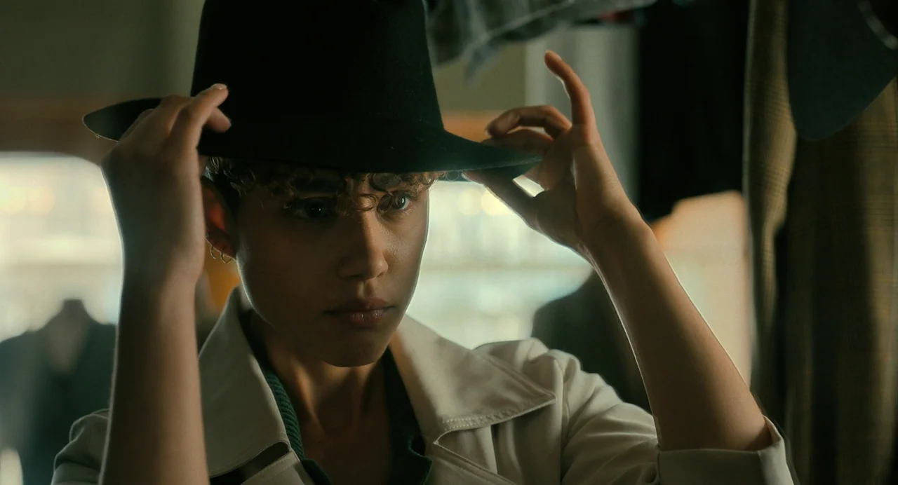 The Killer (2024) (2024) movie still: closeup — An indoor retail space with racks of clothing visible in the blurred background. A young woman looks…