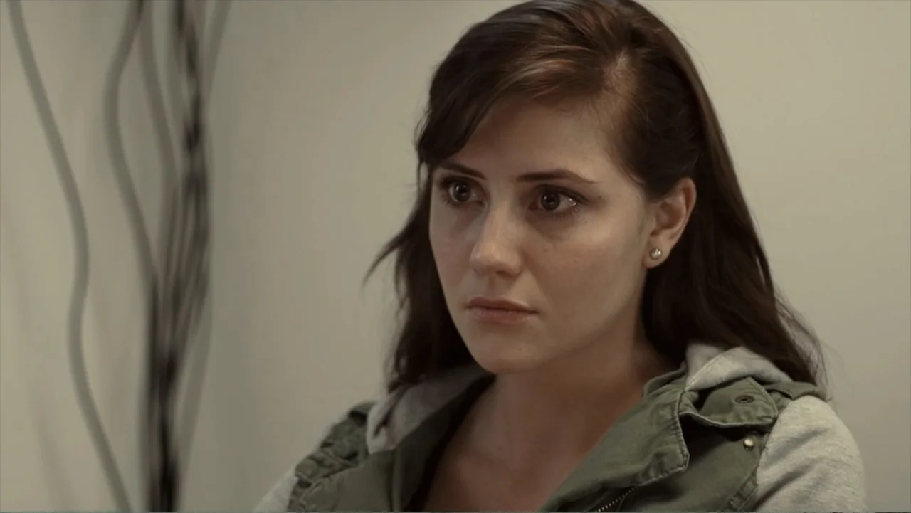 Hello I Love You (2018) movie still: closeup — An interior space with a neutral-colored wall and dark abstract vertical lines. A young woman in an…