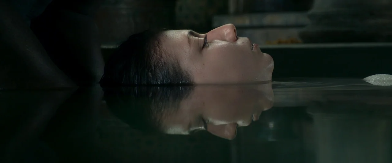 Three Thousand Years of Longing (2022) movie still: closeup — A dark, dimly lit environment features a person lying in deep, still water. The water…