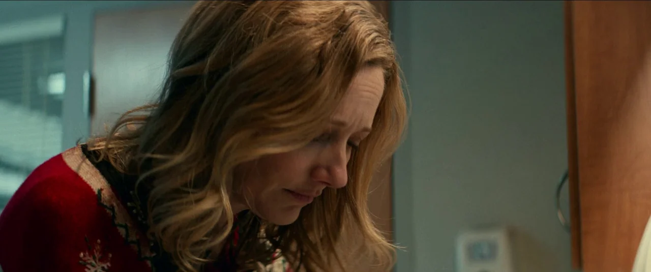 Halloween Kills (2021) movie still: closeup — A woman stands in a sterile space with muted blue-grey walls. The woman wears a red patterned sweater…