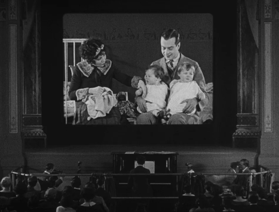 Sherlock Jr. (1924) movie still: wide — A silent film audience sits in a theater watching a movie on a screen. The projected film shows a man and…