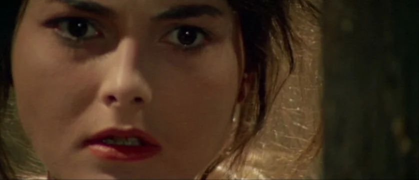 Django Kill (1967) movie still: closeup — A close-up shot of a woman in a dimly lit, nondescript interior space. She stares directly forward with…