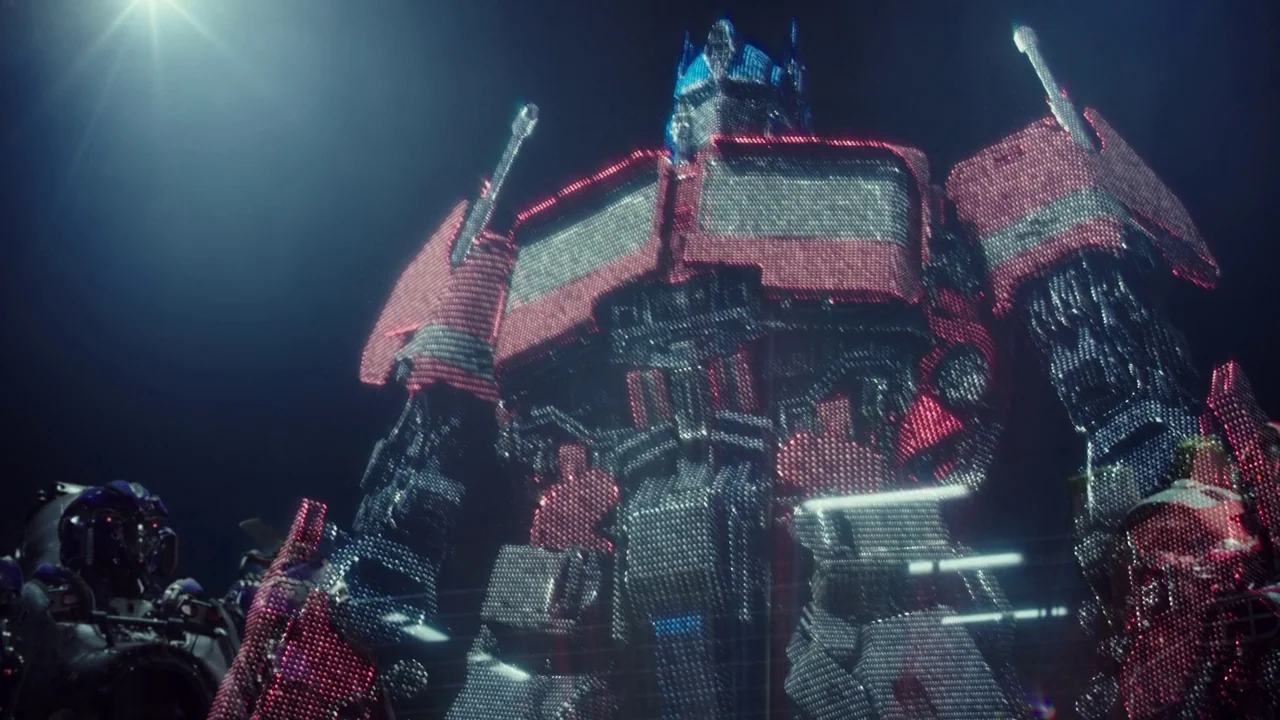 Bumblebee (2018) movie still: fullbody — A group of giant metallic robotic figures stand against a dark, featureless background environment. The…