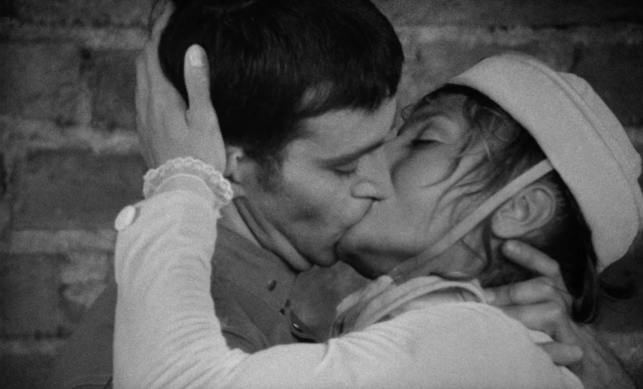 Goto, Island of Love (1969) movie still: closeup — A man and a woman embrace and kiss in front of a textured brick wall. The tight frame excludes…