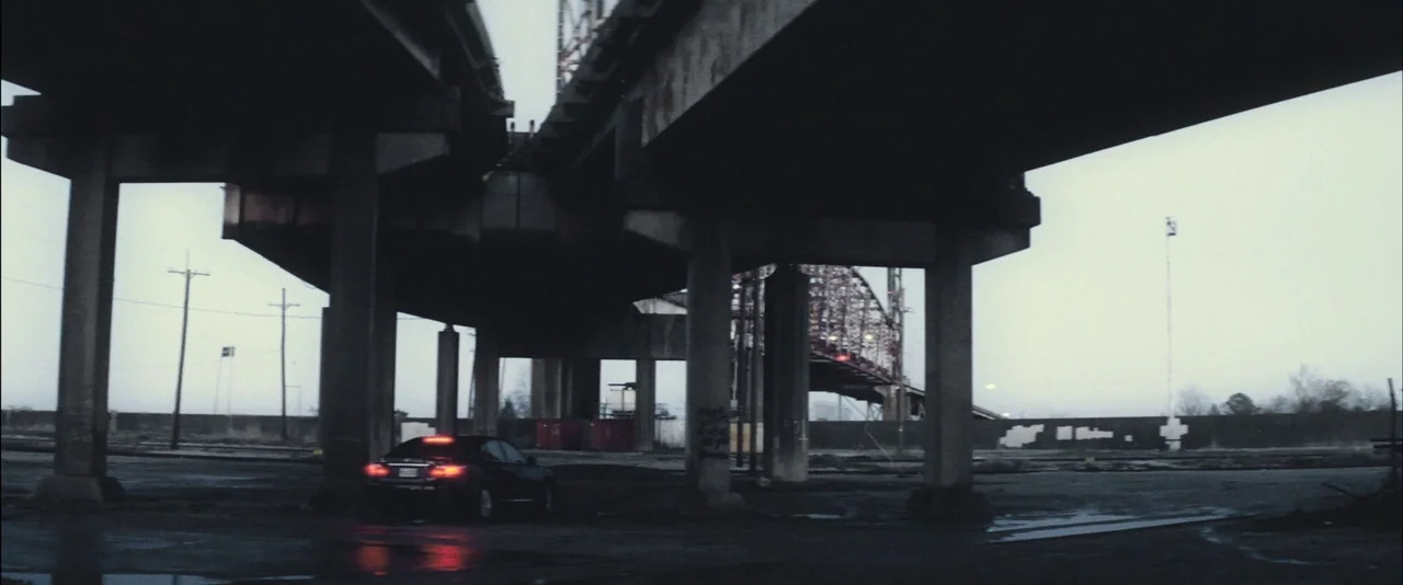 Killing Them Softly (2012) movie still: wide — A desolate area beneath a sprawling concrete overpass structure stands on a grey day. A solitary…