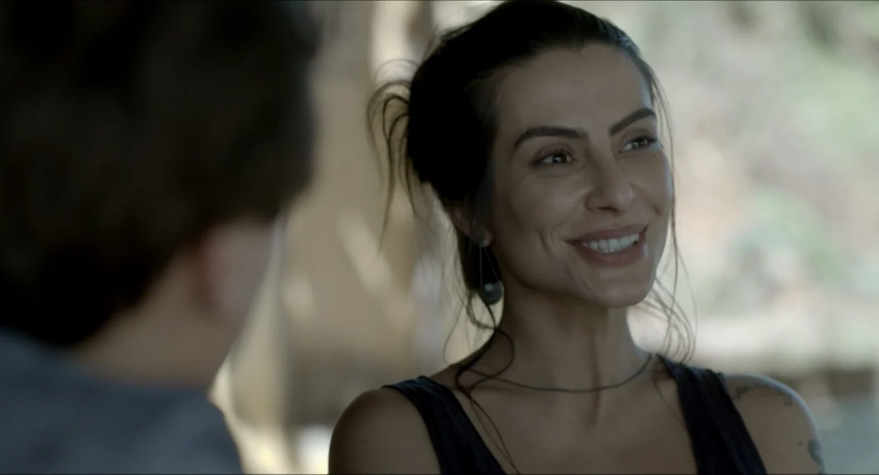 Suspension Points (2022) movie still: closeup — An outdoor area with blurred foliage visible in the naturalistic background lighting. A woman with…