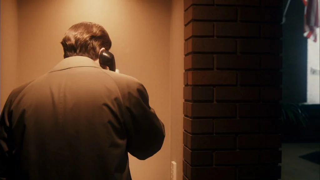 The Informant! (2009) movie still: medium — An interior lobby space featuring a vertical brick pillar on the right. A man stands facing a wall while…