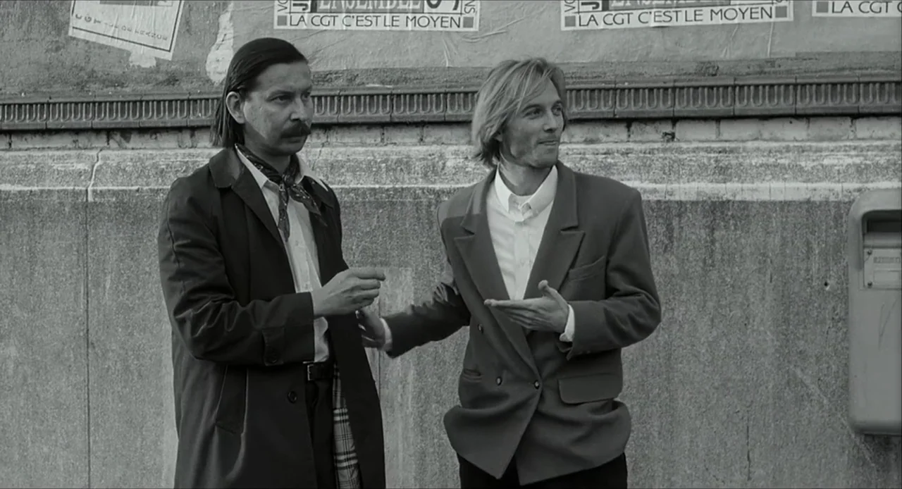 The Bohemian Life (1945) movie still: medium — Two men stand before a textured concrete wall covered in French political posters. One man in a…