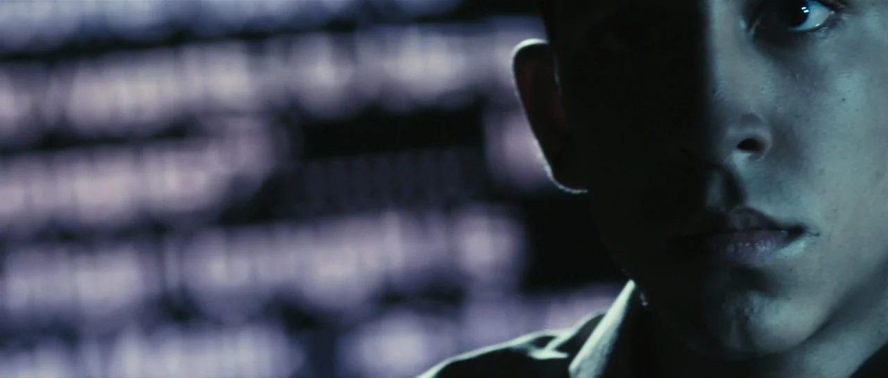 Slumdog Millionaire (2008) movie still: closeup — A man's face is lit from the side by an unseen glowing digital screen. The background is…