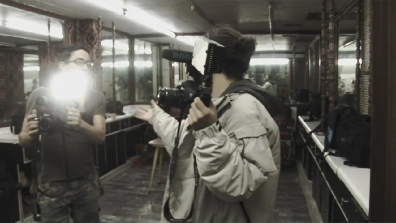 Lost (2010) movie still: medium — A long room lined with mirrors and wooden frame panels contains two camera operators. The two people stand facing…