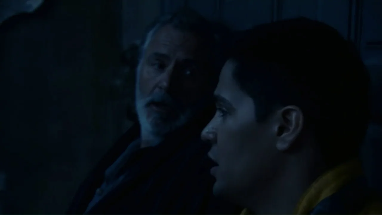 Quarantine (2008) movie still: medium — A dimly lit interior space with very low visibility and deep blue shadows. An older man and a younger man…