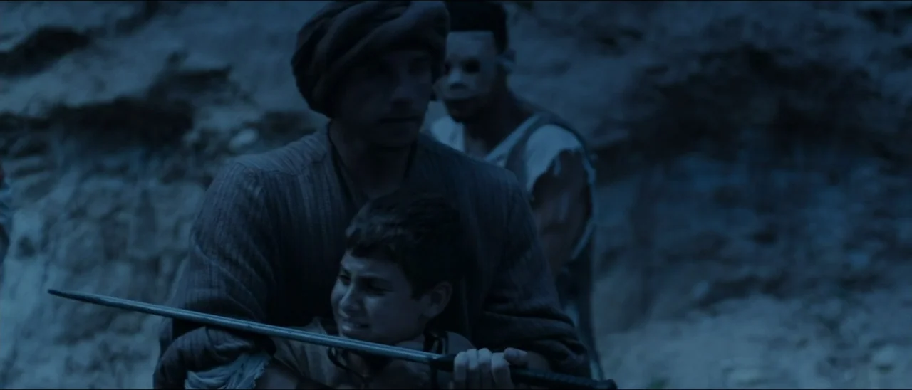 The Penitent Thief (2021) movie still: medium — A rocky exterior landscape at night features uneven terrain with textured stone surfaces. A man…