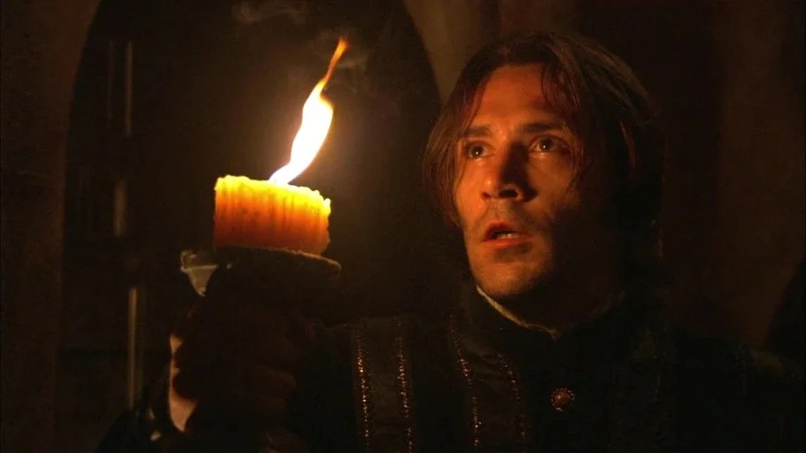 The Tudors (2007) movie still: closeup — A dark stone space is lit only by the flickering flame of a candle. A man looks ahead with a wide-eyed…