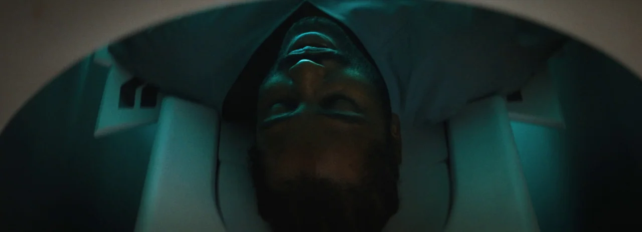 The Creator (2023) movie still: closeup — A man lies on his back inside the circular aperture of an MRI machine. His head is positioned centrally…