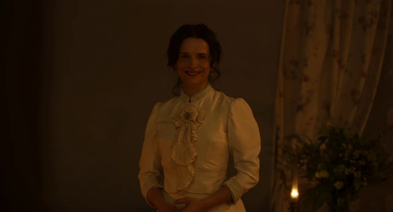 The Taste of Things (2023) movie still: medium — A dimly lit room with a floral curtain visible in the blurry background. A woman in a Victorian…