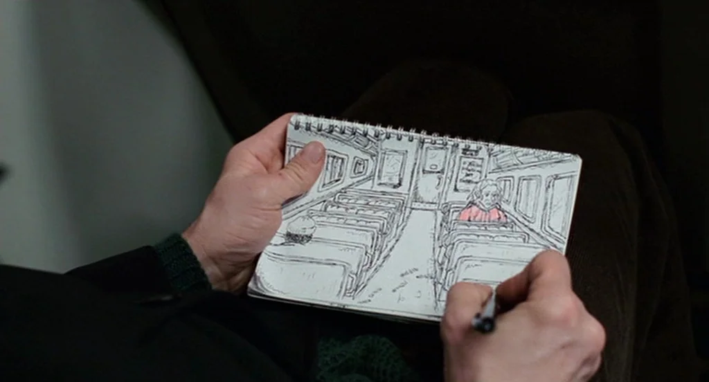 Eternal Sunshine of the Spotless Mind (2004) movie still: closeup — A person holds a sketchbook showing an ink drawing of a train passenger cabin.…