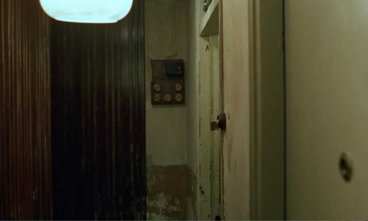 In the Mood for Love (2000) movie still: establishing — A narrow apartment corridor features weathered walls and a central electrical fuse box. No…