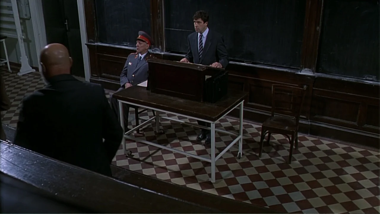 Citizen X (1995) movie still: medium — A wood-paneled room features checkered floor tiles and a prominent chalkboard backdrop. Three men stand in…