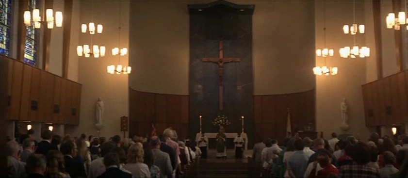 Nashville (1975) movie still: wide — A church sanctuary featuring wood-paneled walls and a central altar with a crucifix wall piece. A large…