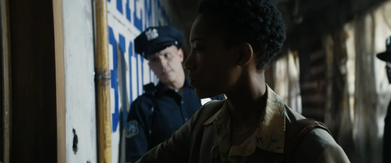 Dogman (2023) movie still: medium — An interior space with peeling paint and worn walls featuring a faded police sign. A young woman stands looking…