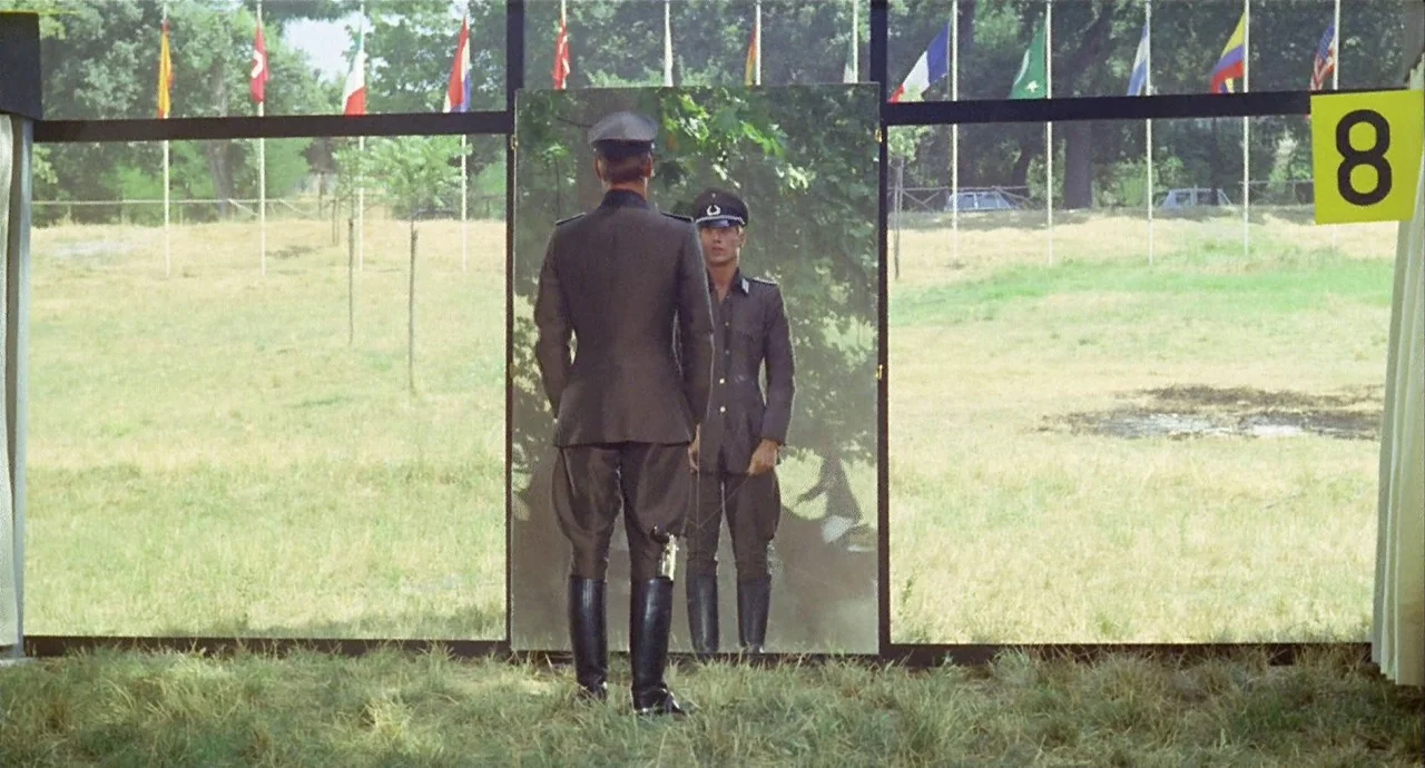 The 10th Victim (1965) movie still: fullbody — A man in a military uniform stands before a tall standing mirror outdoors. He looks at his own…