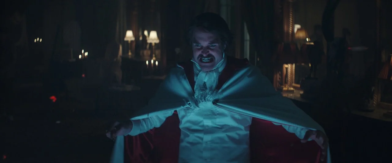 Extra Ordinary (2019) movie still: medium — A dimly lit room contains multiple lamps and candles set against dark furniture. A man in period…