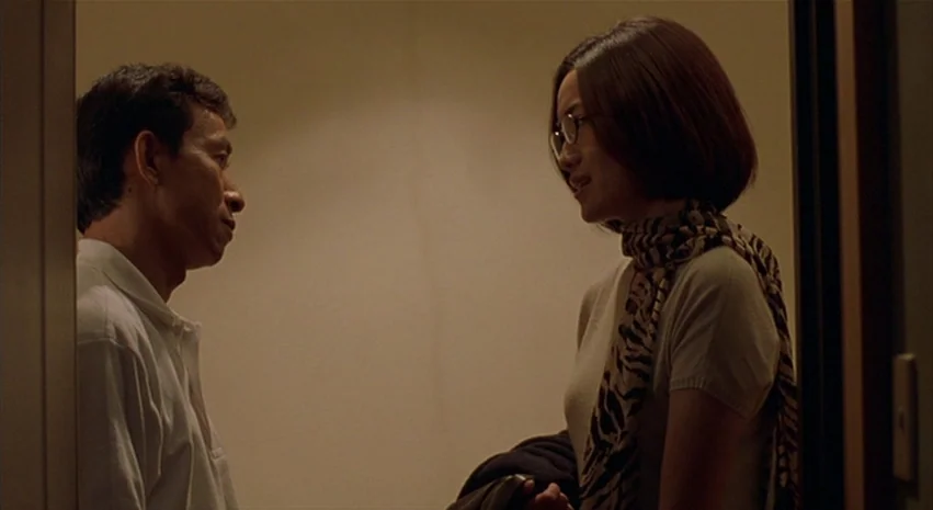 Yi-Yi (A One and A Two) (2000) movie still: medium — Two individuals stand within a narrow doorway against a plain, dimly lit wall. They face each…