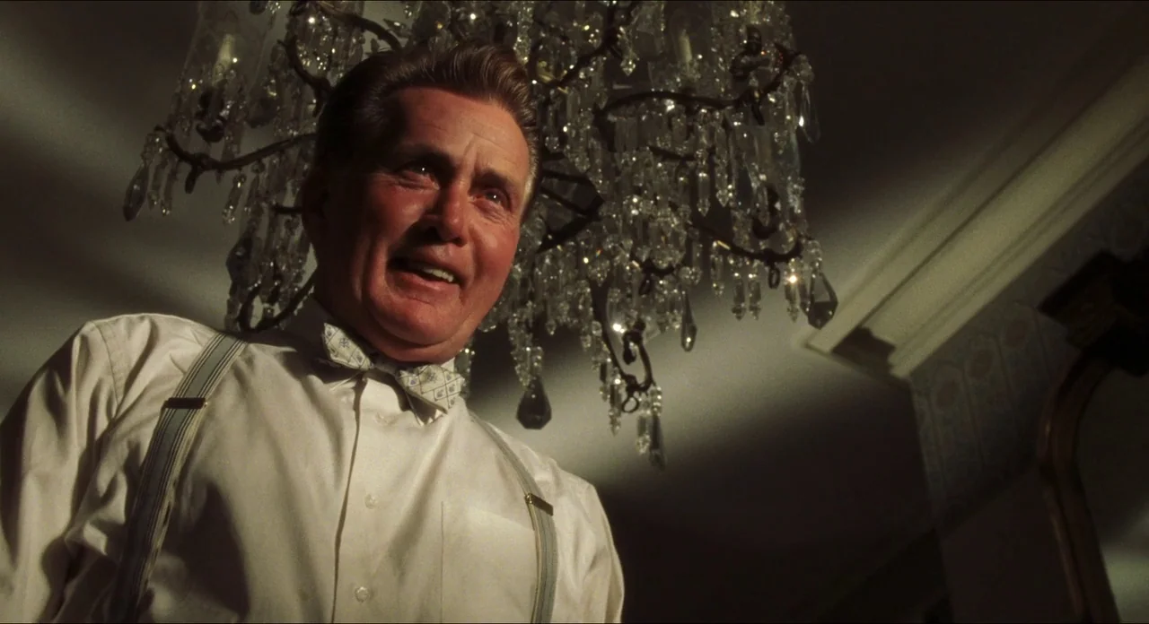 Catch Me If You Can (2002) movie still: medium — A dimly lit hotel space features a large crystal chandelier hanging directly above a man. The man…