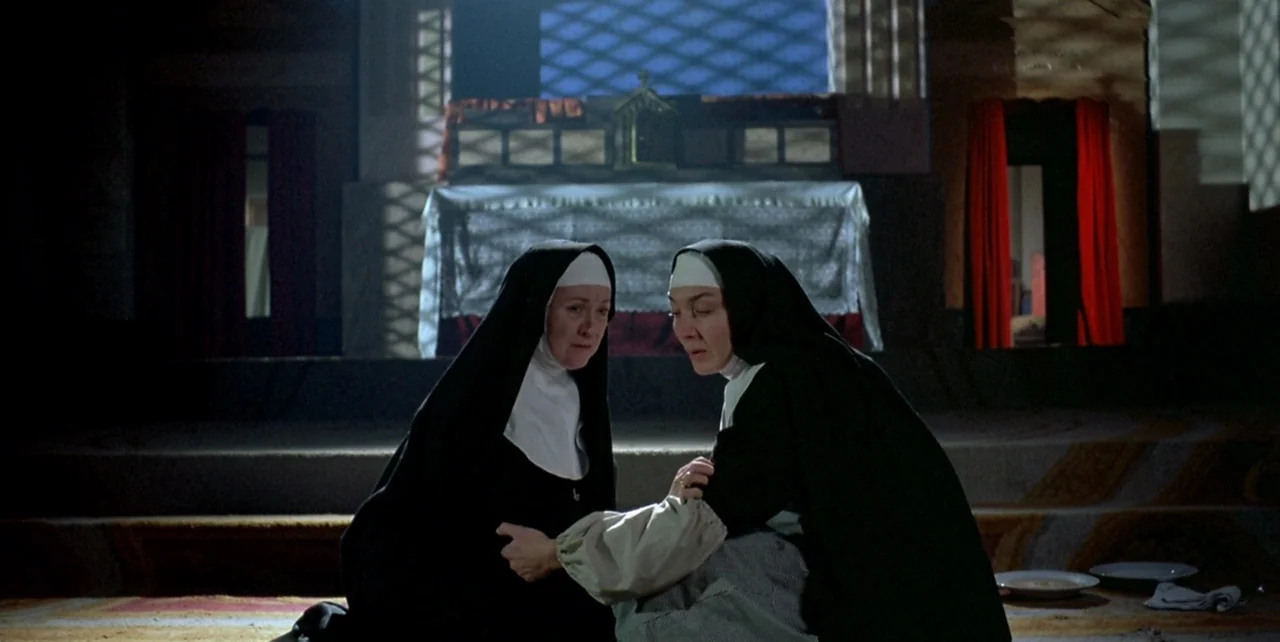 Dark Habits (1983) movie still: medium — A dimly lit religious interior features a stone altar draped in white cloth. Two nuns kneel together on the…