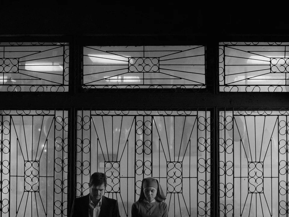 Ida (2013) movie still: medium — Two individuals stand in front of a large decorative metal security gate. The background behind the grating is…