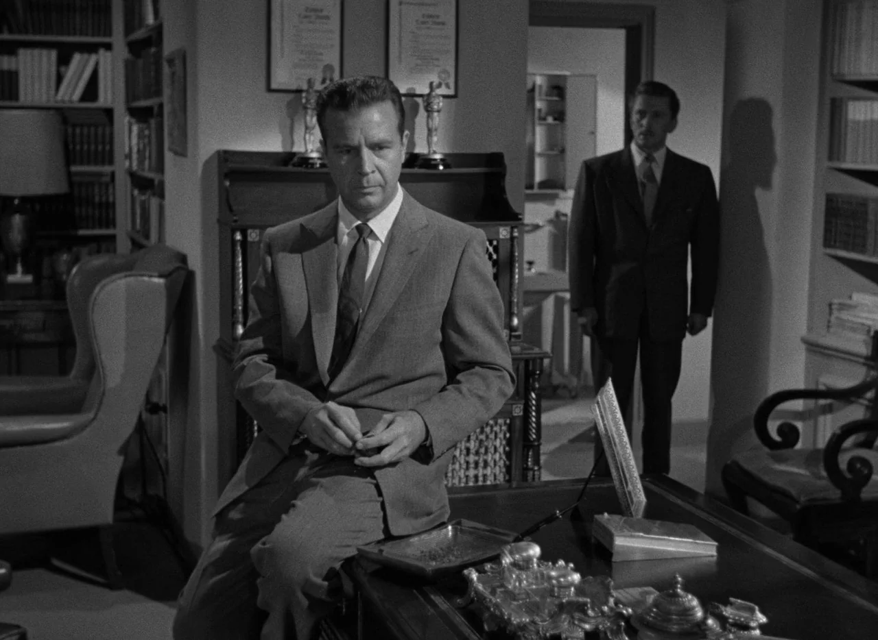The Bad and the Beautiful (1952) movie still: medium — A study filled with bookshelves, framed awards, and a cluttered dark wooden desk. One man…