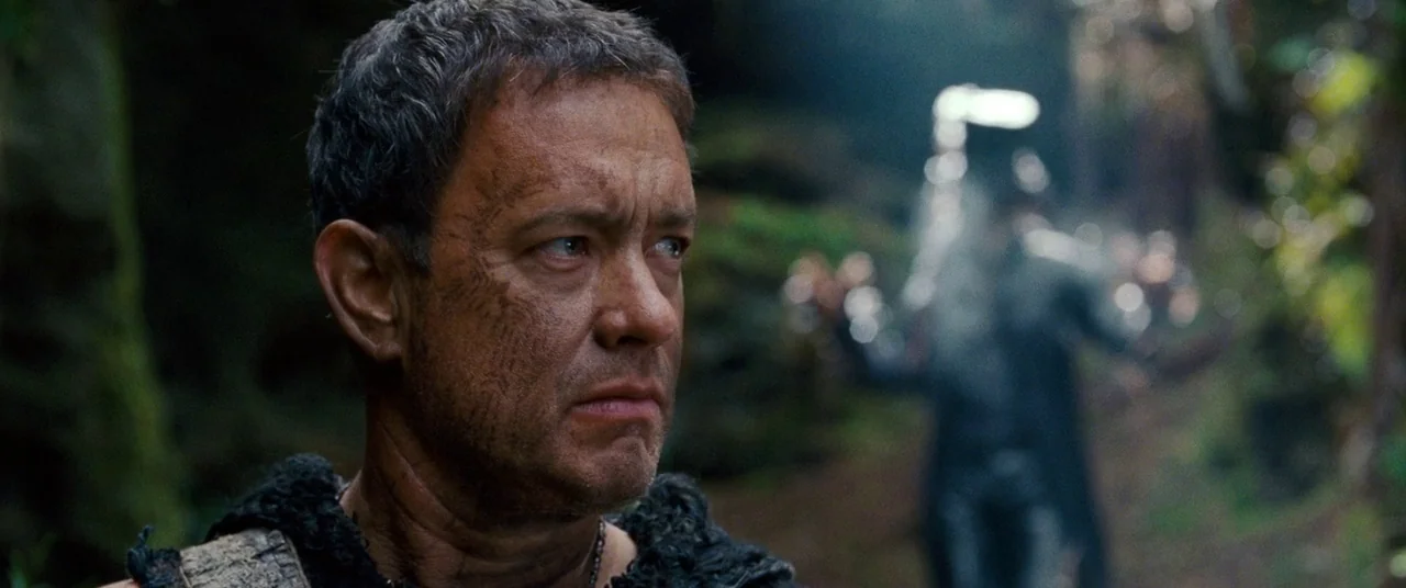Cloud Atlas (2012) movie still: closeup — A dense, shadowed woodland path with soft, filtered sunlight breaking through the leafy canopy. A man with…