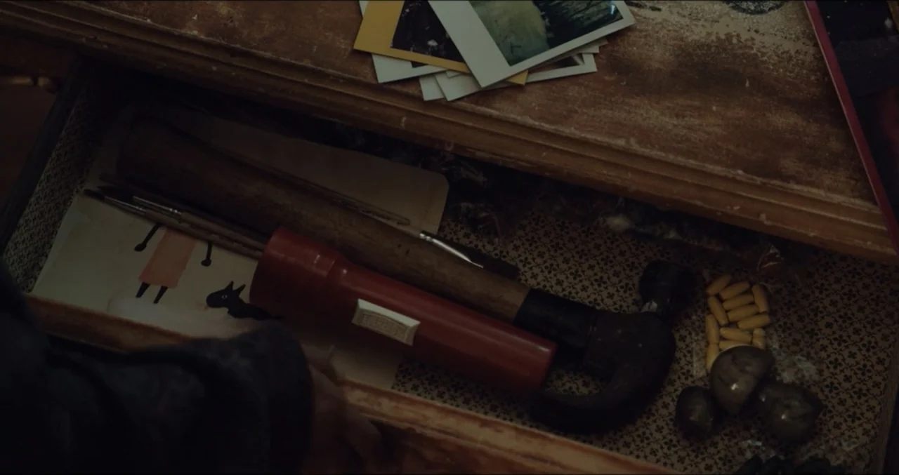 Eye for an Eye (2025) movie still: closeup — An open wooden drawer features patterned lining paper and various personal items inside. A hand pulls…