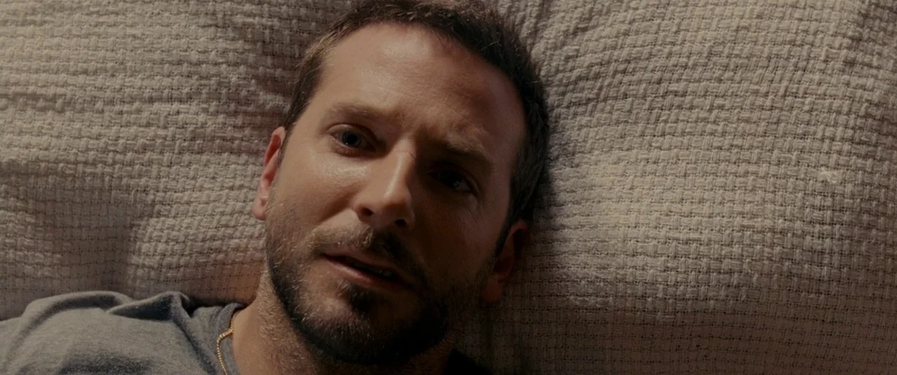 Silver Linings Playbook (2012) movie still: closeup — A man lies on a textured, light-colored fabric surface that covers his head area. He is…