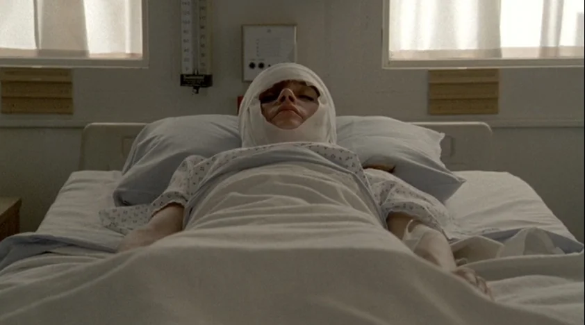 The House Of The Devil (2009) movie still: medium — A stark hospital room features a white bed against a clinical, featureless wall. A patient lies…