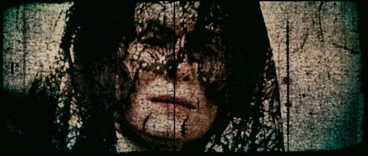 Silent Hill movie still: closeup — A dark, heavily textured frame shows a person behind a black lace veil. The subject stares ahead through the mesh…