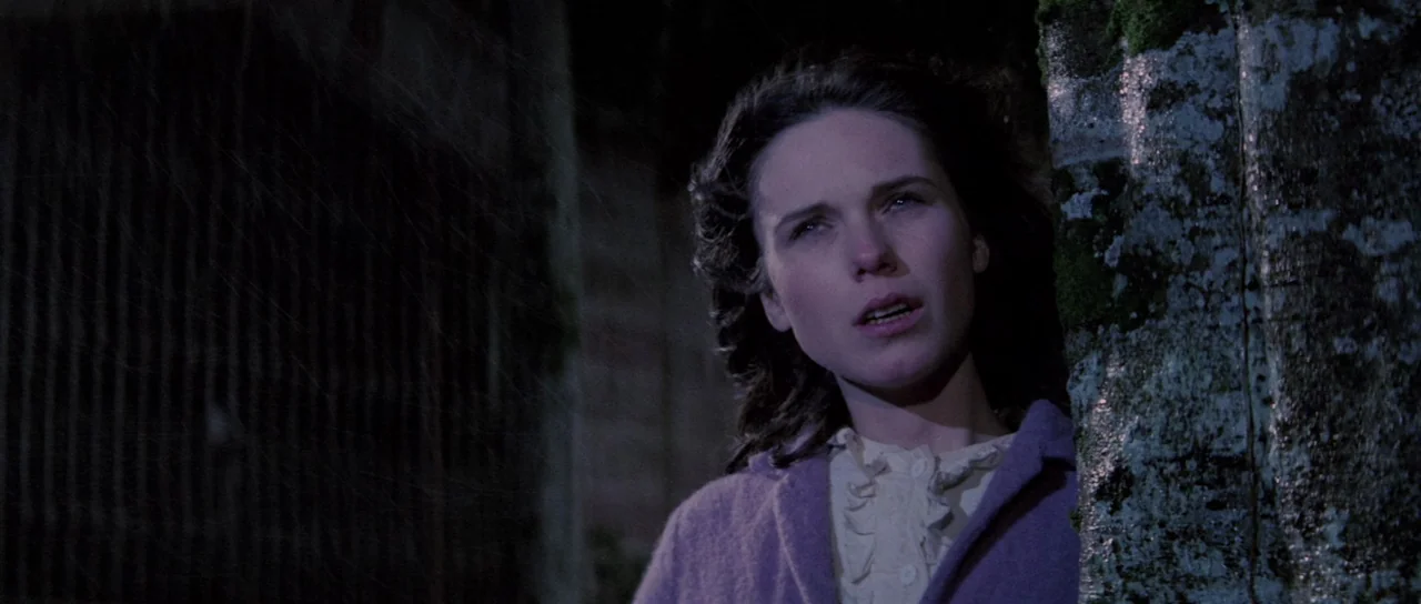 The House That Screamed (1969) movie still: medium — A dark, wet outdoor setting features a textured stone wall covered in patches of moss. A woman…