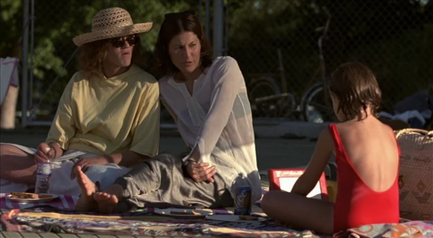 Being John Malkovich (1999) movie still: medium — A poolside concrete area features a colorful blanket spread over the ground. Two adult women talk…
