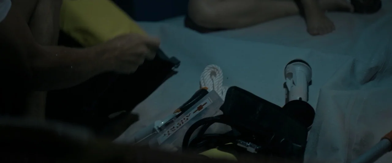 Great White (1998) movie still: closeup — A dark boat deck surface holds a collection of survival and first aid gear. Various medical supplies and…