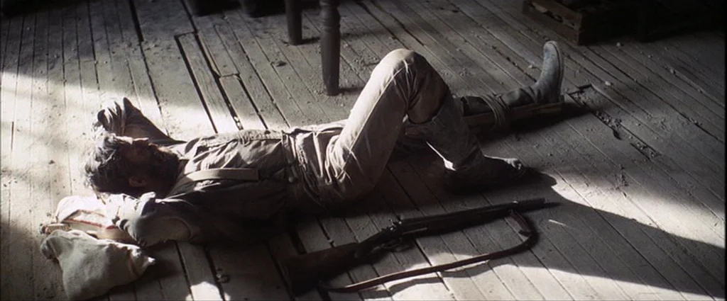 There Will Be Blood (2007) movie still: fullbody — A dusty wooden floor shows worn planks and debris from a structural gap. A man lies on his back…