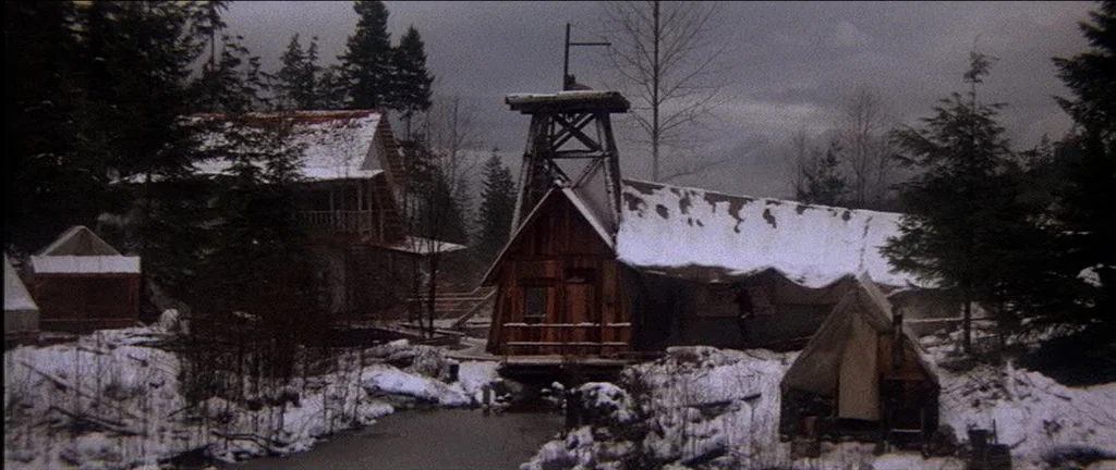 McCabe & Mrs.Miller (1971) movie still: establishing — A remote, snow-dusted mining camp features wooden cabins and a central elevated hoist…